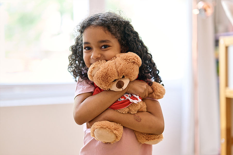 Ein Mädchen freut sich und kuschelt mit einem Teddybär.