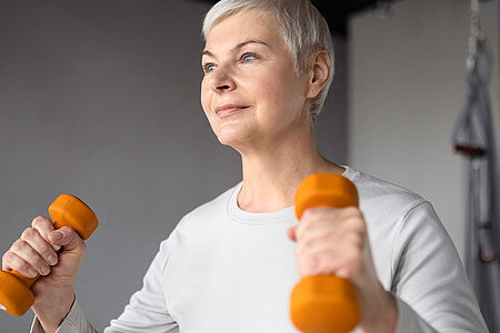 Ältere Frau trainiert beim Functional Training mit zwei Hanteln.