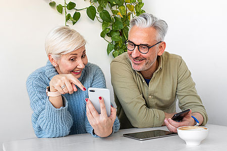 Zwei ältere Menschen probieren gemeinsam digitale Anwendungen auf Smartphone und Tablet aus.